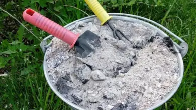 Kbelík s popílkem a zahradními nástroji na trávníku.